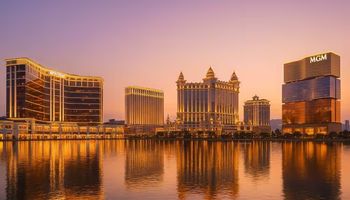 A photo-realistic nighttime view of the Macau skyline with illuminated casinos, reflecting on the water.