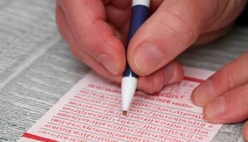 A hand filling out a sports betting slip, with horse racing odds visible in the background,