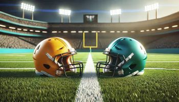 Two football helmets, one yellow-orange and the other teal, placed on a green football field with white yard lines.
