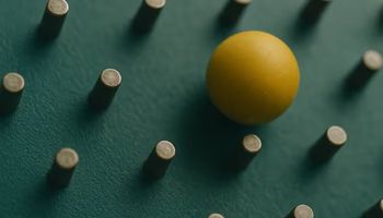 Close-up of a yellow ball bouncing among metal pegs on a teal Plinko board, captured mid-motion with shallow depth of field.