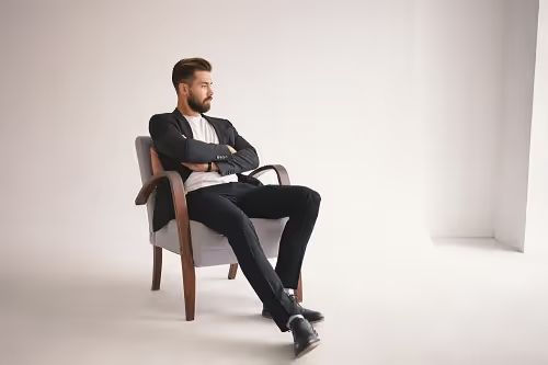 indoor portrait handsome young male lawyer with thick beard trendy hairstyle sitting comfortably armchair keeping arms crossed chest looking away with pensive thoughtful expression 1 1