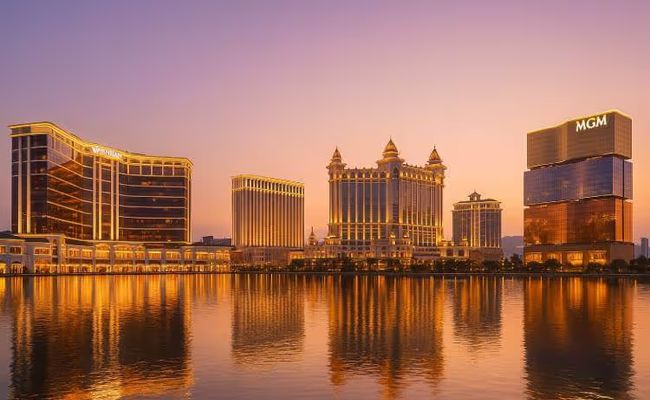 A photo-realistic nighttime view of the Macau skyline with illuminated casinos, reflecting on the water.